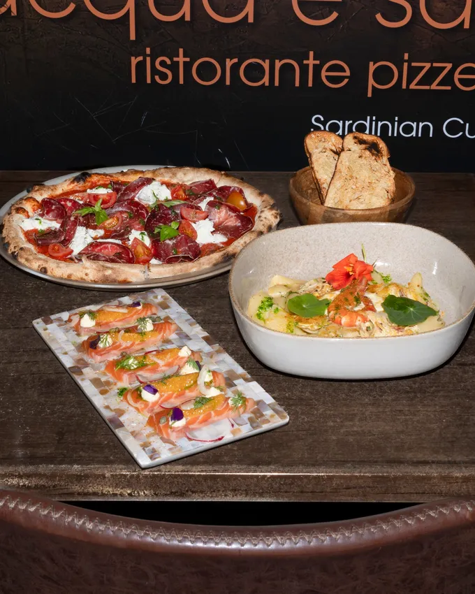 Pizza, pasta and crudo laid out under the Acqua e Sale sign